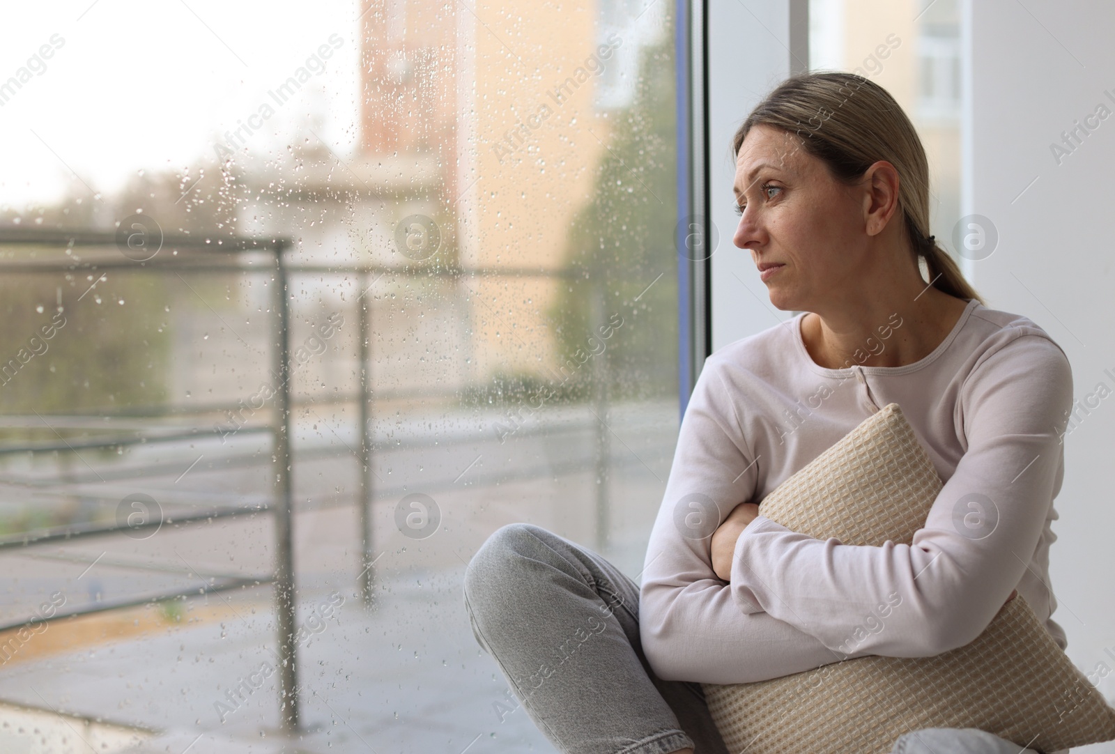 Depressed woman looking out window at home, space for text Photo of Depressed woman looking out window at home, space for text