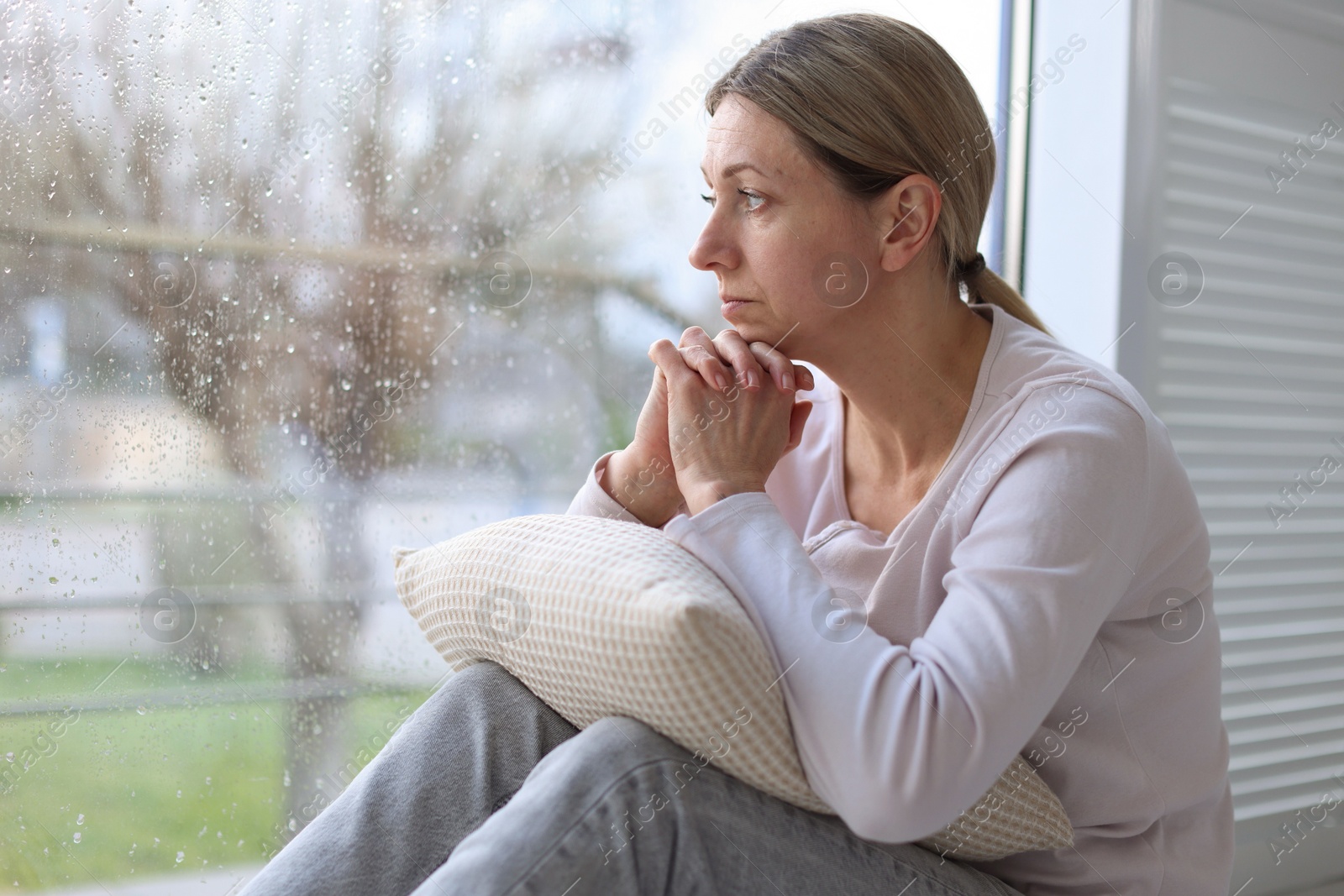 Depressed woman looking out window at home, space for text Photo of Depressed woman looking out window at home, space for text