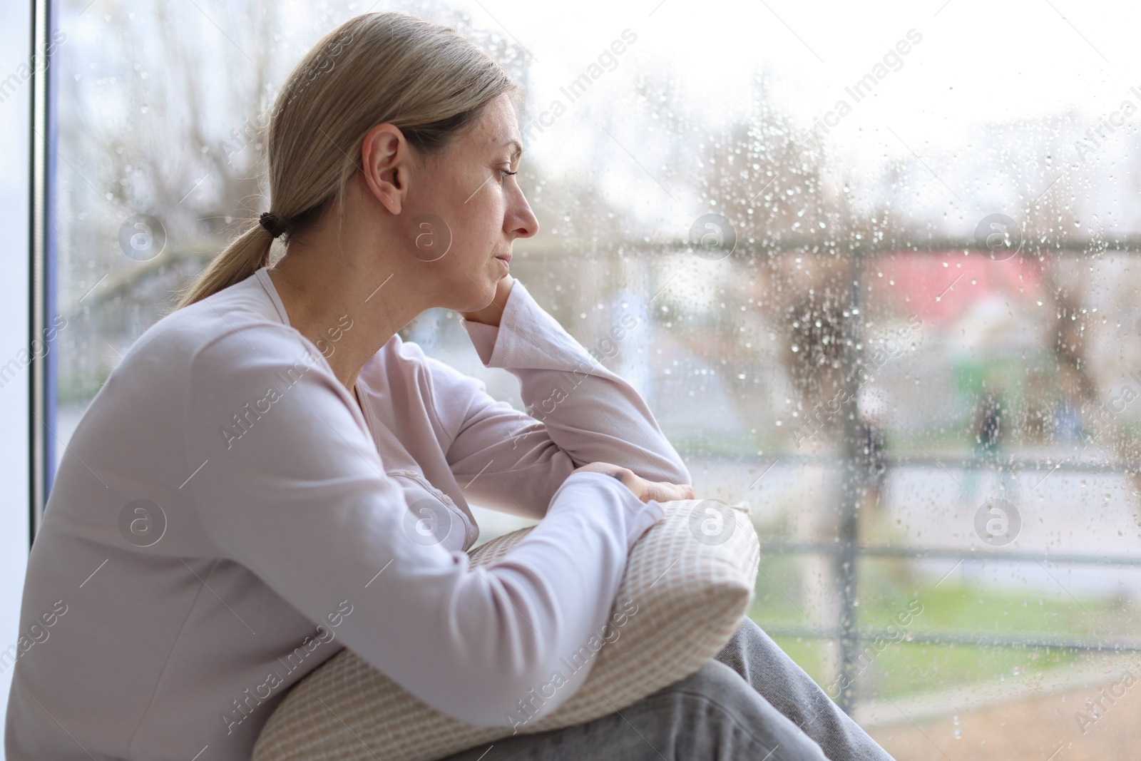 Depressed woman looking out window at home, space for text Photo of Depressed woman looking out window at home, space for text