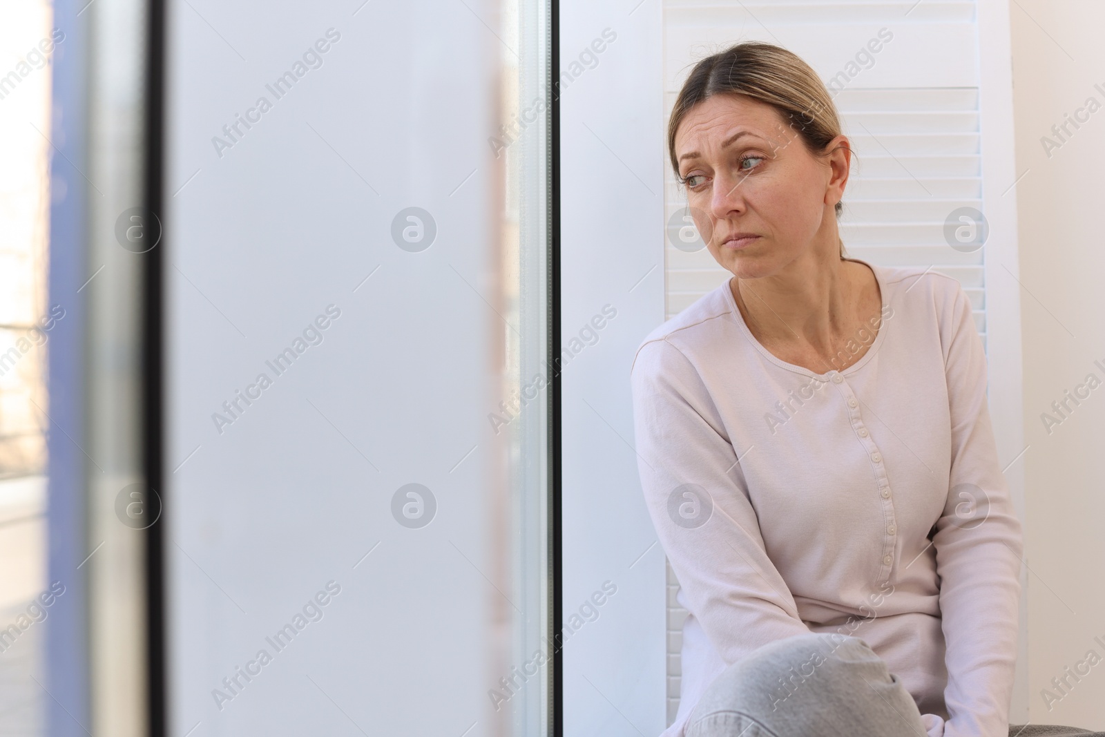 Depressed woman looking out window at home, space for text Photo of Depressed woman looking out window at home, space for text