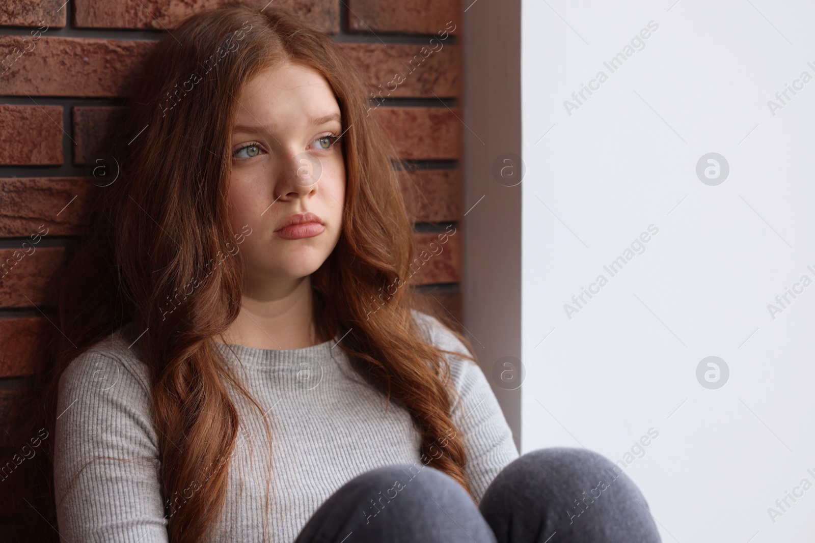 Sad teenage girl near brick wall indoors Photo of Sad teenage girl near brick wall indoors