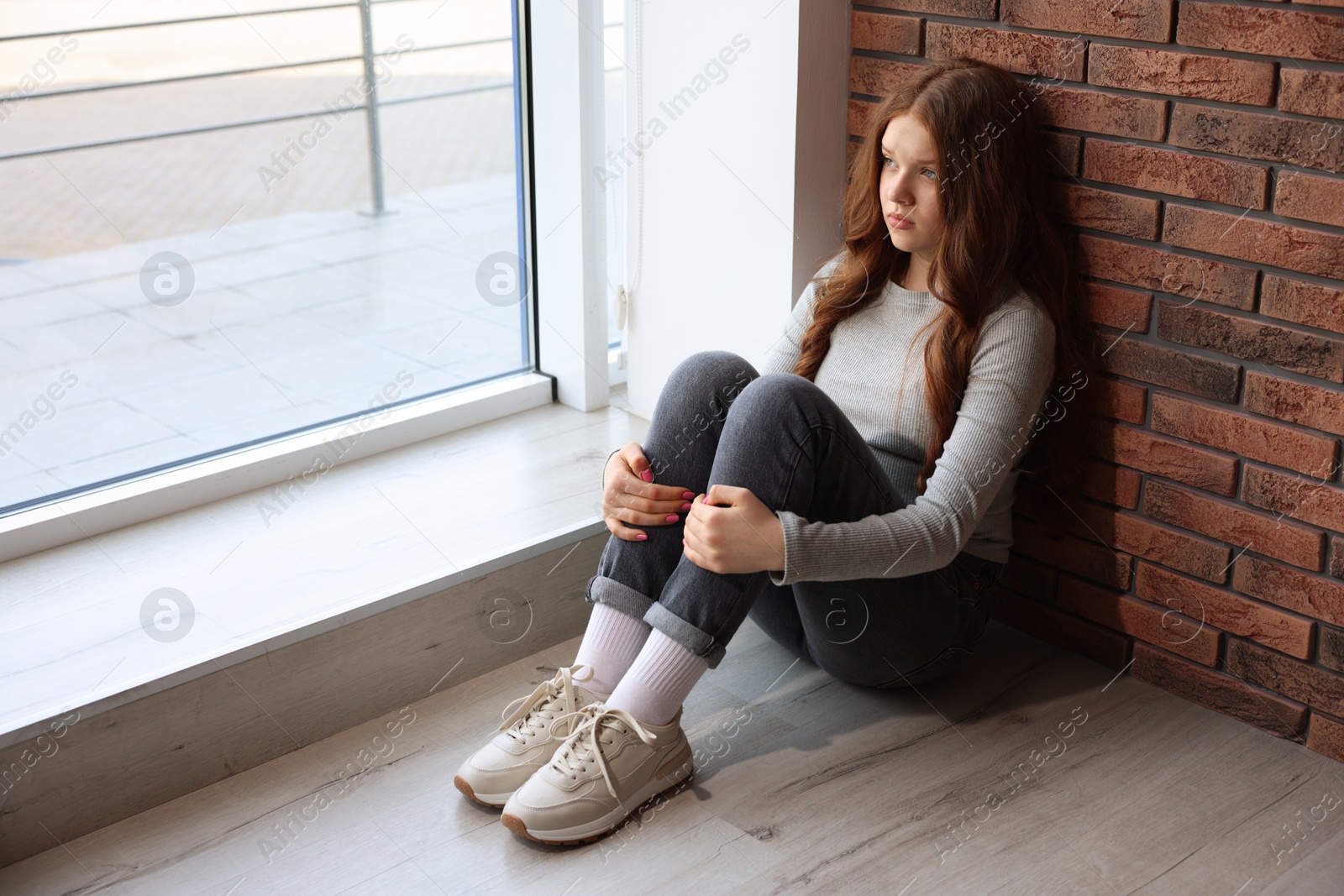 Sad teenage girl near window at home Photo of Sad teenage girl near window at home