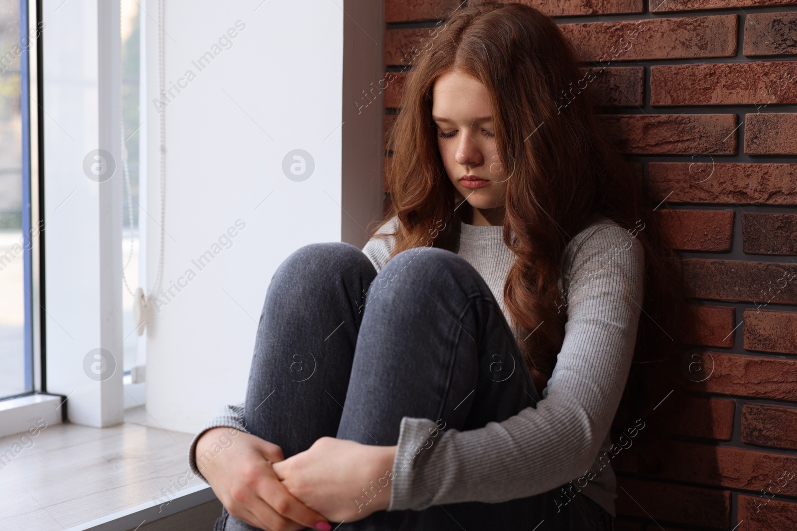 Sad teenage girl near window at home Photo of Sad teenage girl near window at home