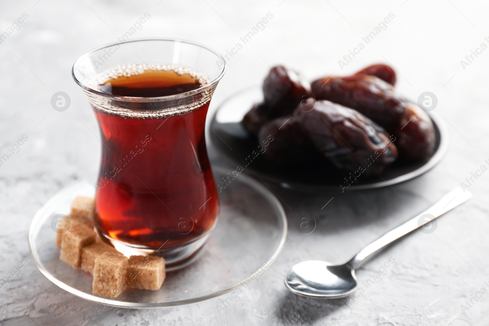 Traditional Turkish tea in glass cup, brown sugar and dates on light grey table, closeup Photo of Traditional Turkish tea in glass cup, brown sugar and dates on light grey table, closeup