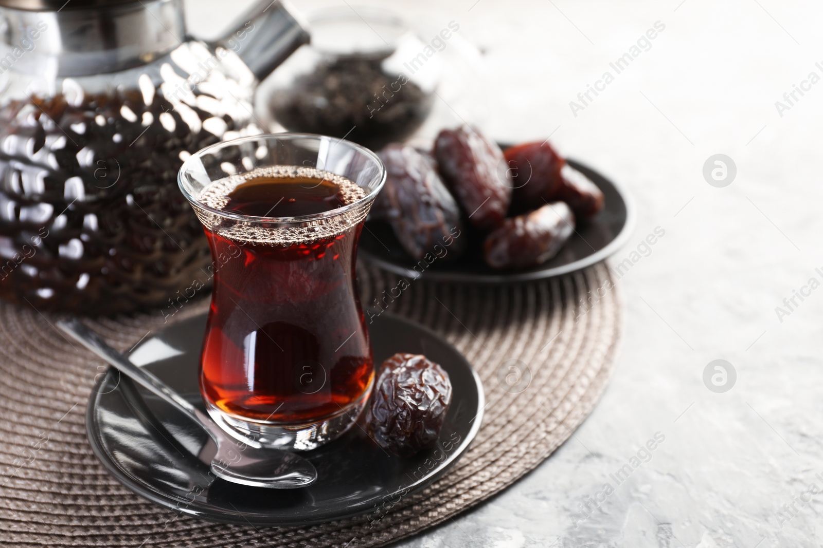 Traditional Turkish tea in glass cup, teapot and dates on light grey table, closeup. Space for text Photo of Traditional Turkish tea in glass cup, teapot and dates on light grey table, closeup. Space for text