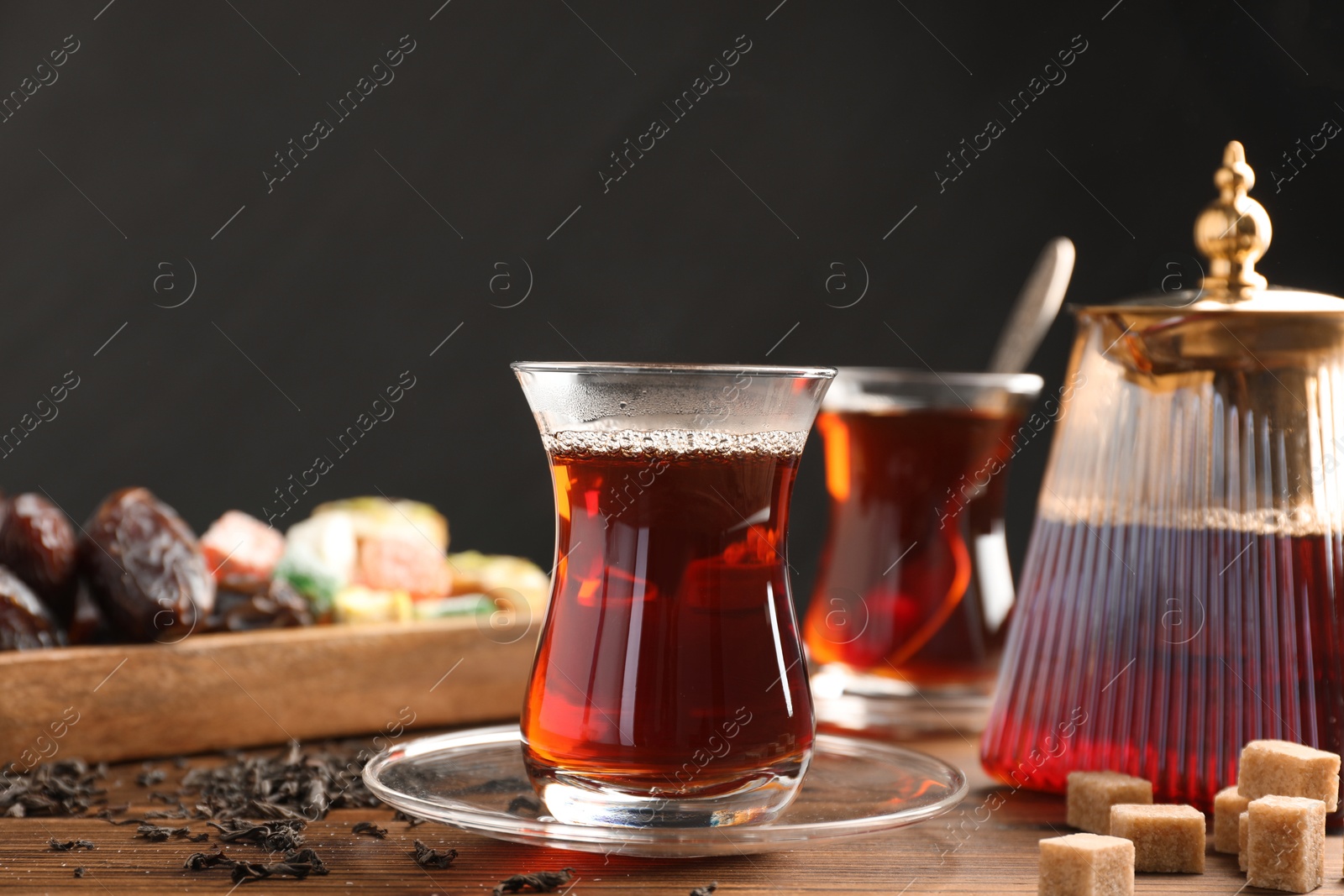 Traditional Turkish tea in glass cups, teapot, dry leaves, brown sugar and sweets on wooden table, closeup Photo of Traditional Turkish tea in glass cups, teapot, dry leaves, brown sugar and sweets on wooden table, closeup