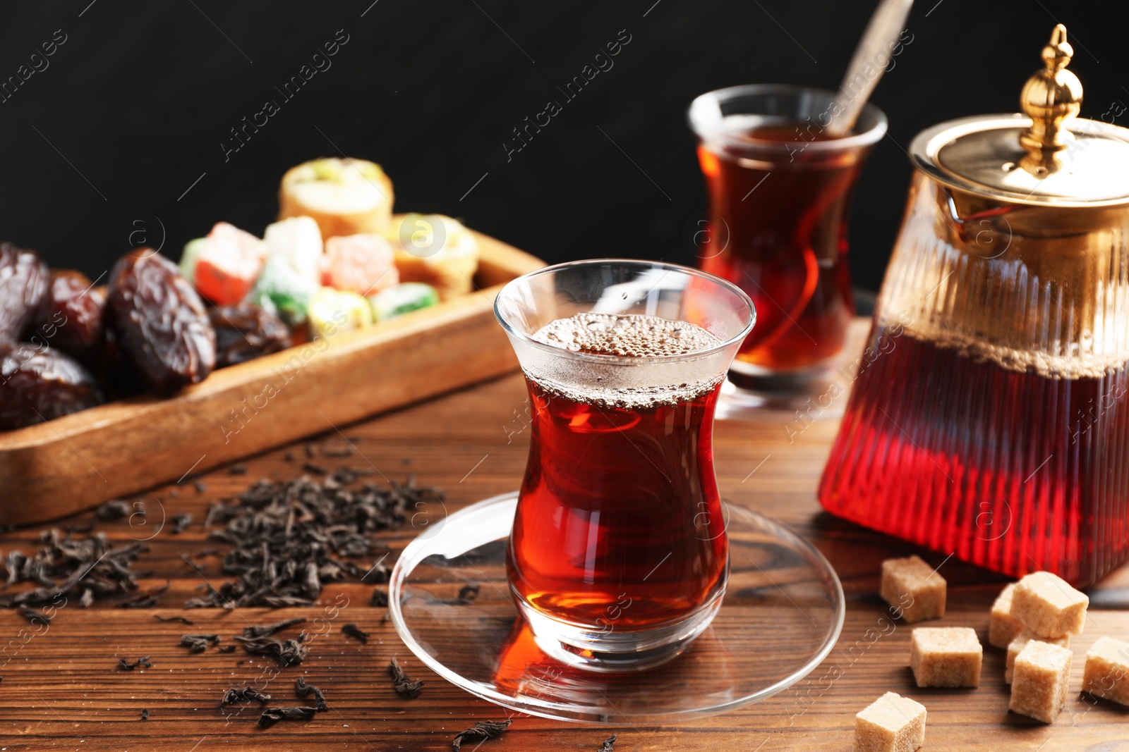Traditional Turkish tea in glass cups, teapot, dry leaves, brown sugar and sweets on wooden table, closeup Photo of Traditional Turkish tea in glass cups, teapot, dry leaves, brown sugar and sweets on wooden table, closeup