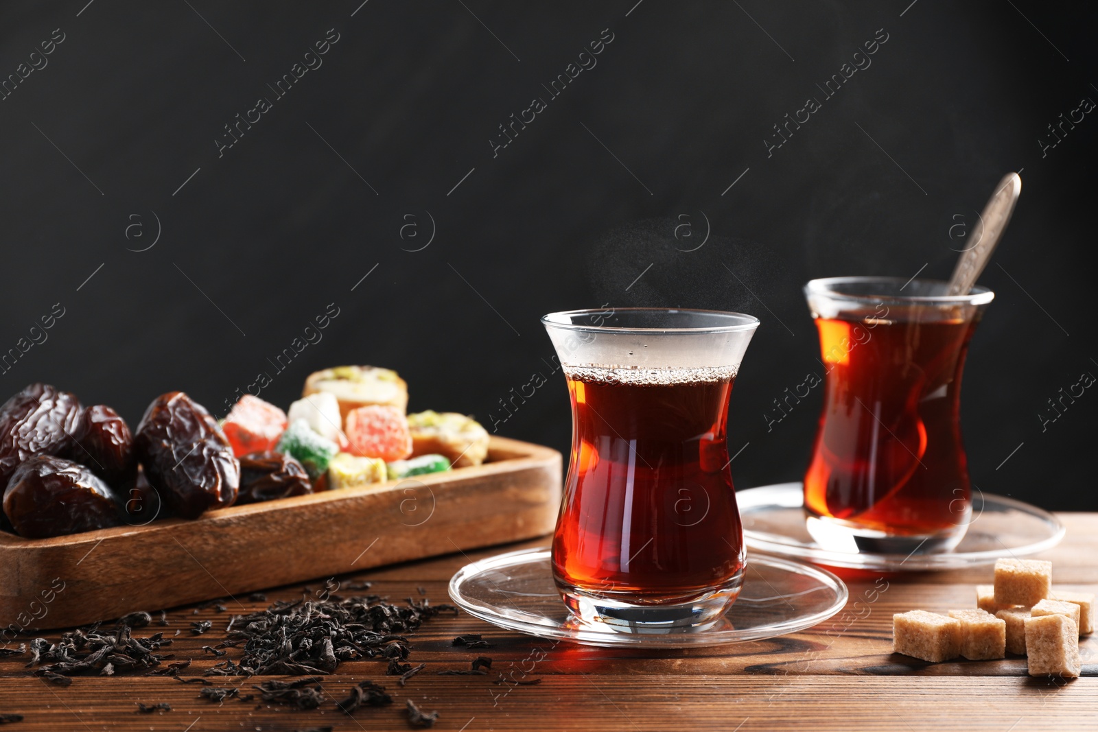 Traditional Turkish tea in glass cups, dry leaves, brown sugar and sweets on wooden table, closeup Photo of Traditional Turkish tea in glass cups, dry leaves, brown sugar and sweets on wooden table, closeup