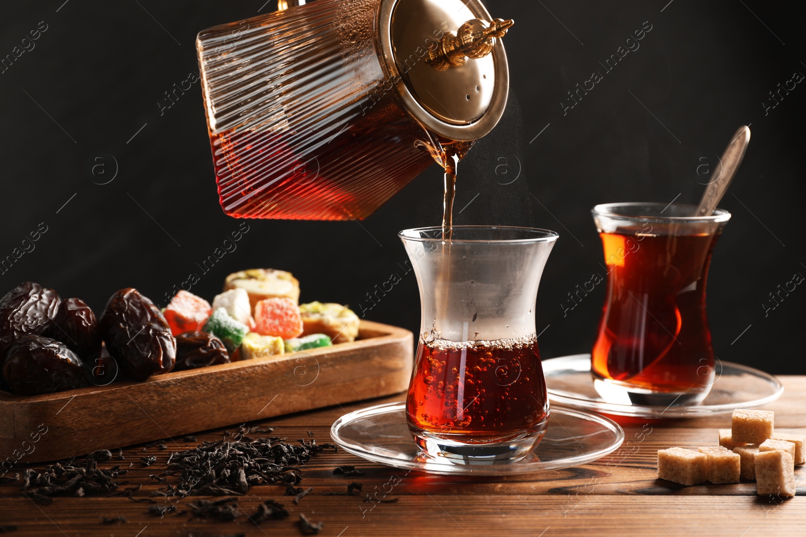 Pouring Turkish tea into glass cup at wooden table, closeup Photo of Pouring Turkish tea into glass cup at wooden table, closeup