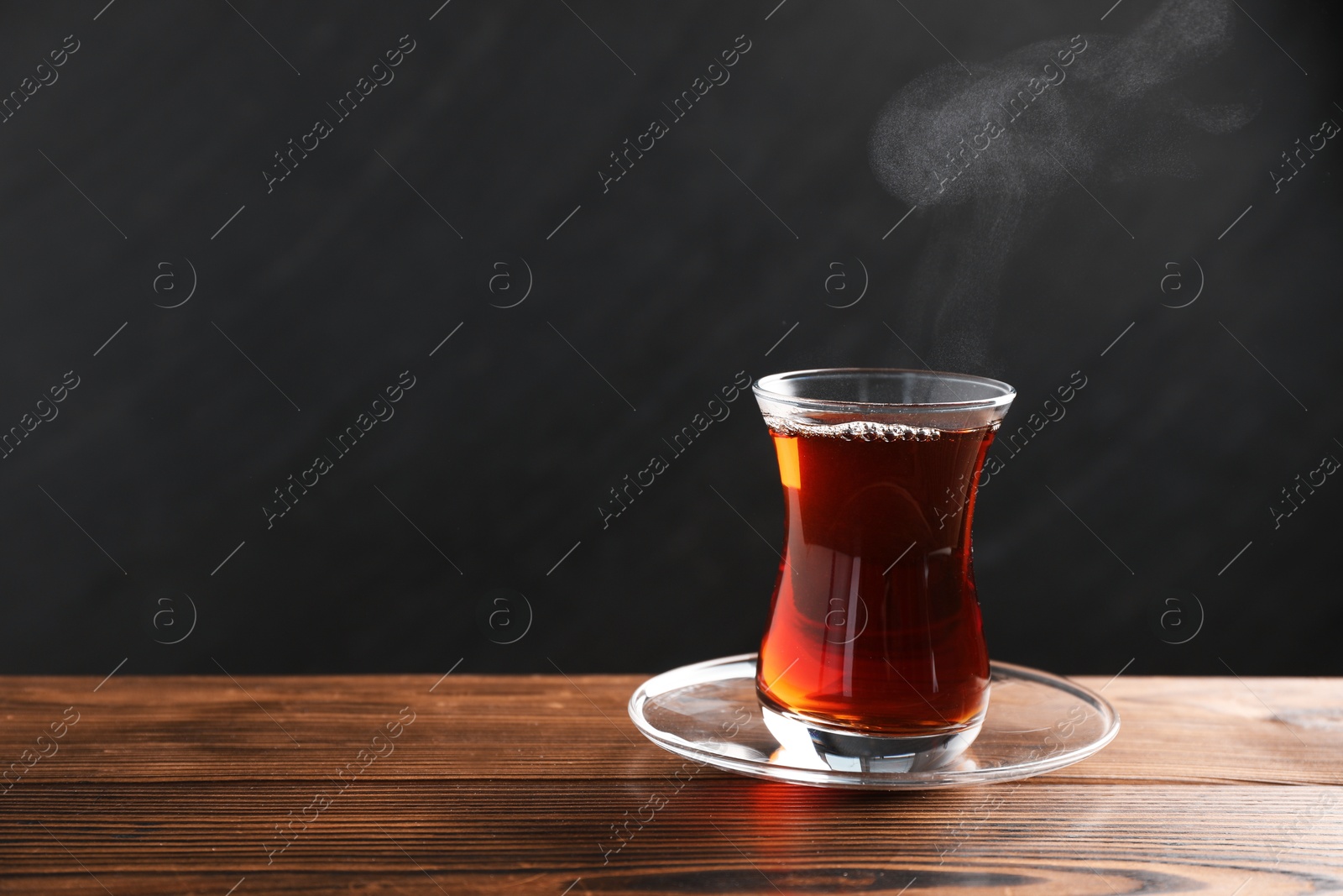 Traditional Turkish tea in glass cup on wooden table, space for text Photo of Traditional Turkish tea in glass cup on wooden table, space for text
