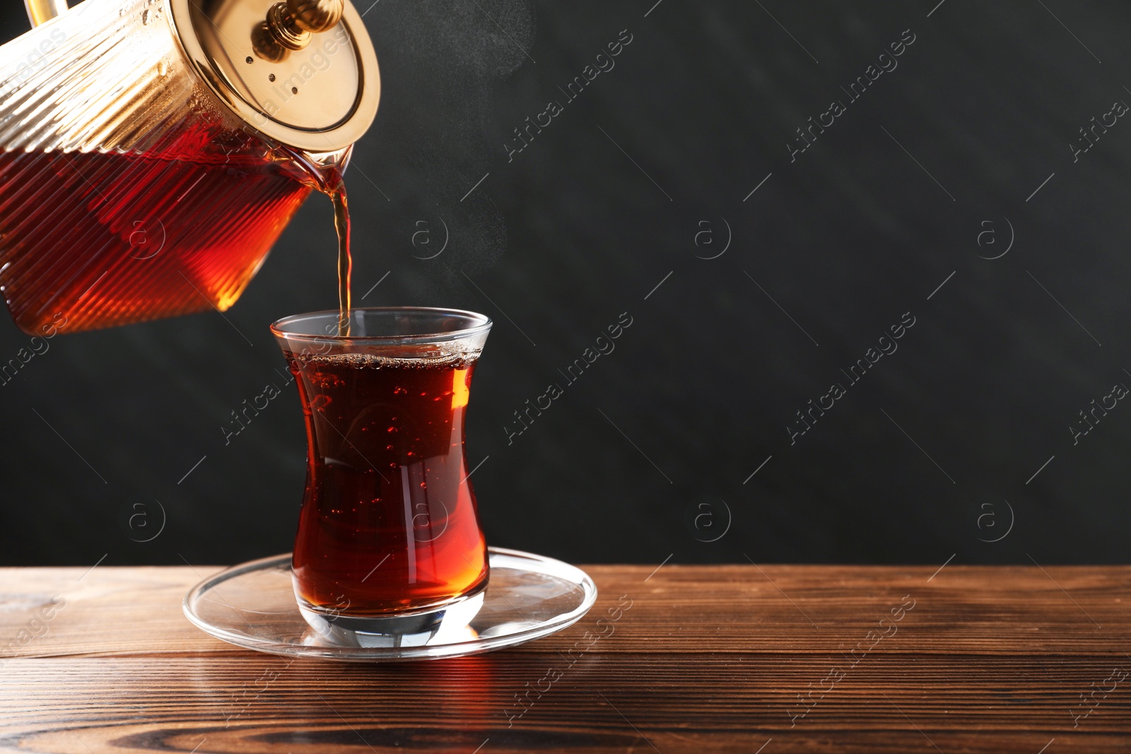 Pouring Turkish tea into glass cup at wooden table, closeup. Space for text Photo of Pouring Turkish tea into glass cup at wooden table, closeup. Space for text