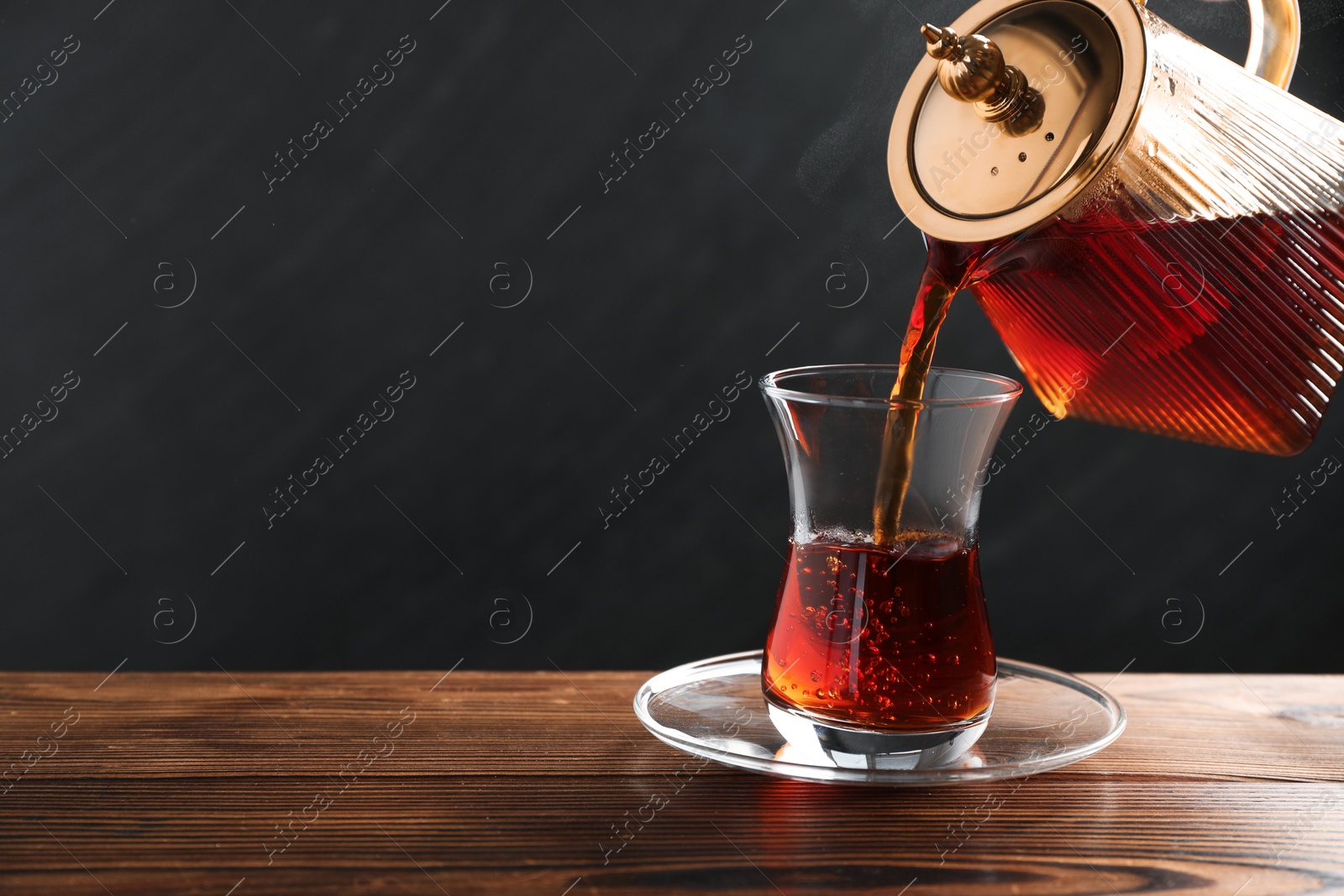 Pouring Turkish tea into glass cup at wooden table, closeup. Space for text Photo of Pouring Turkish tea into glass cup at wooden table, closeup. Space for text