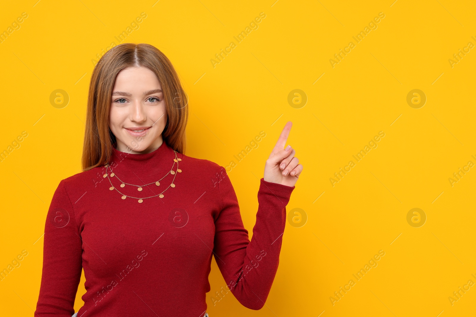 Photo of Portrait of smiling teenage girl pointing at something on yellow background. Space for text