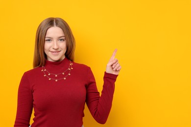 Photo of Portrait of smiling teenage girl pointing at something on yellow background. Space for text