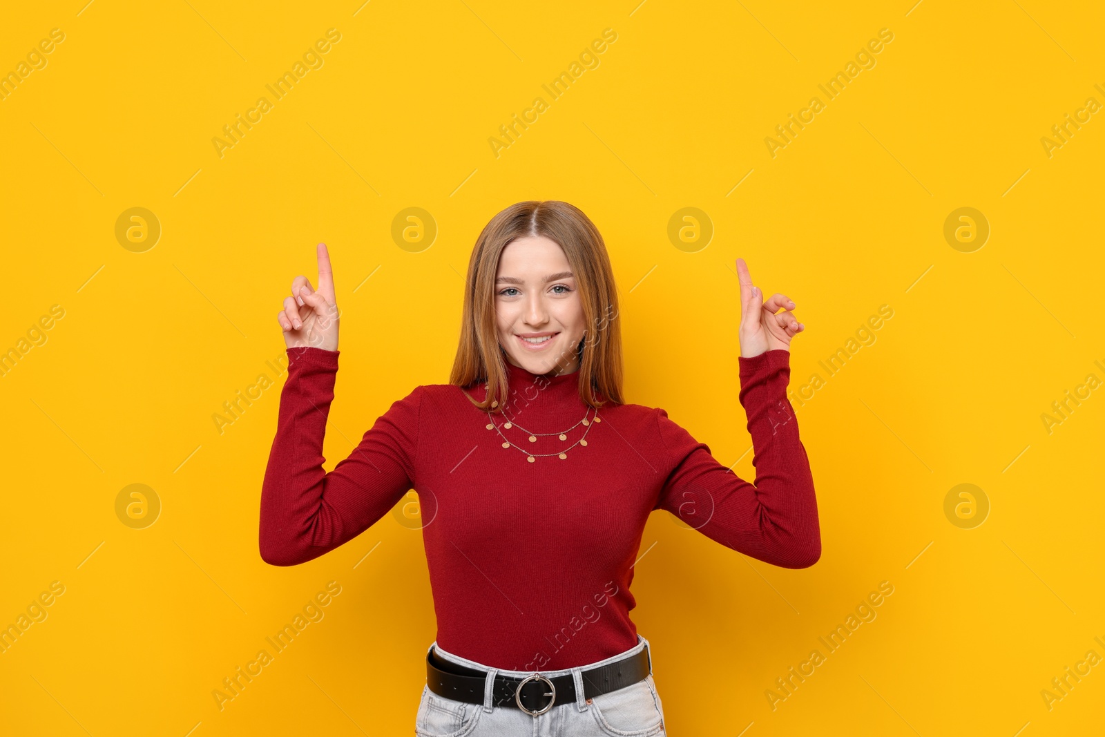 Portrait of smiling teenage girl pointing upwards on yellow background Photo of Portrait of smiling teenage girl pointing upwards on yellow background