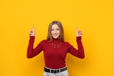 Photo of Portrait of smiling teenage girl pointing upwards on yellow background