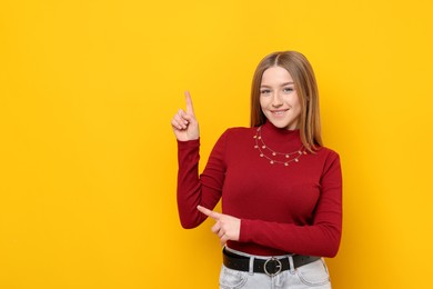 Photo of Portrait of smiling teenage girl pointing at something on yellow background. Space for text