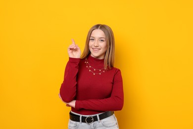 Photo of Portrait of smiling teenage girl pointing upwards on yellow background