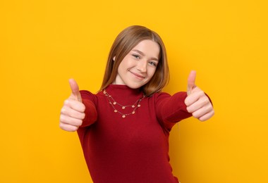 Photo of Portrait of teenage girl showing thumbs up on yellow background