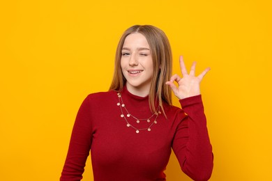 Photo of Portrait of smiling teenage girl showing ok gesture on yellow background
