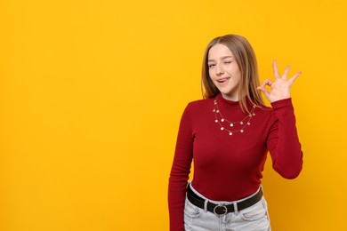 Photo of Portrait of smiling teenage girl showing ok gesture on yellow background. Space for text