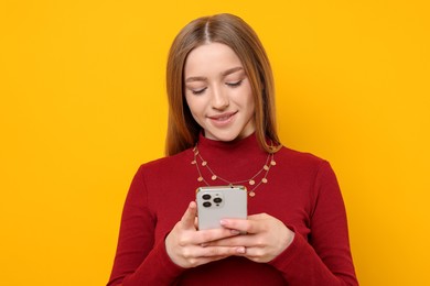 Photo of Smiling teenage girl with smartphone on yellow background
