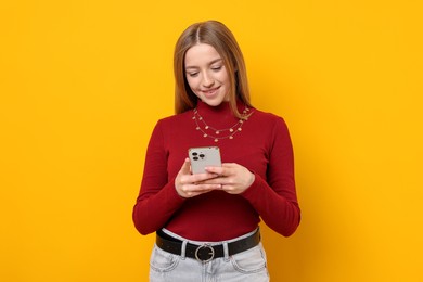 Photo of Smiling teenage girl with smartphone on yellow background