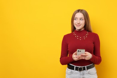 Photo of Smiling teenage girl with smartphone on yellow background. Space for text