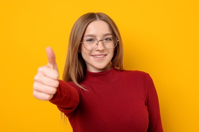 Photo of Portrait of smiling teenage girl showing thumbs up on yellow background