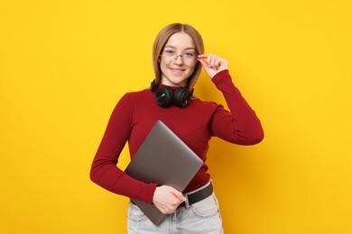 Photo of Smiling teenage girl with laptop on yellow background