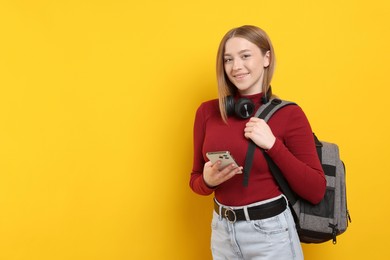 Photo of Smiling teenage girl with smartphone on yellow background. Space for text