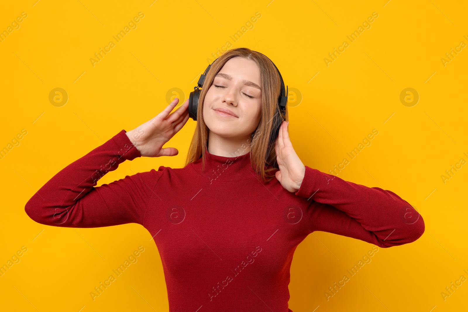 Beautiful teenage girl in headphones listening to music on yellow background Photo of Beautiful teenage girl in headphones listening to music on yellow background