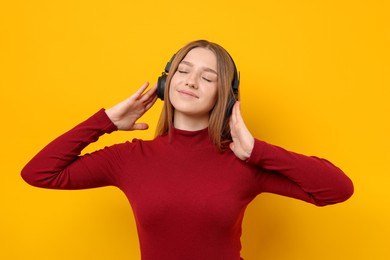 Photo of Beautiful teenage girl in headphones listening to music on yellow background