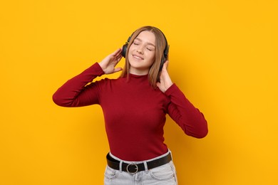 Photo of Smiling teenage girl in headphones listening to music on yellow background