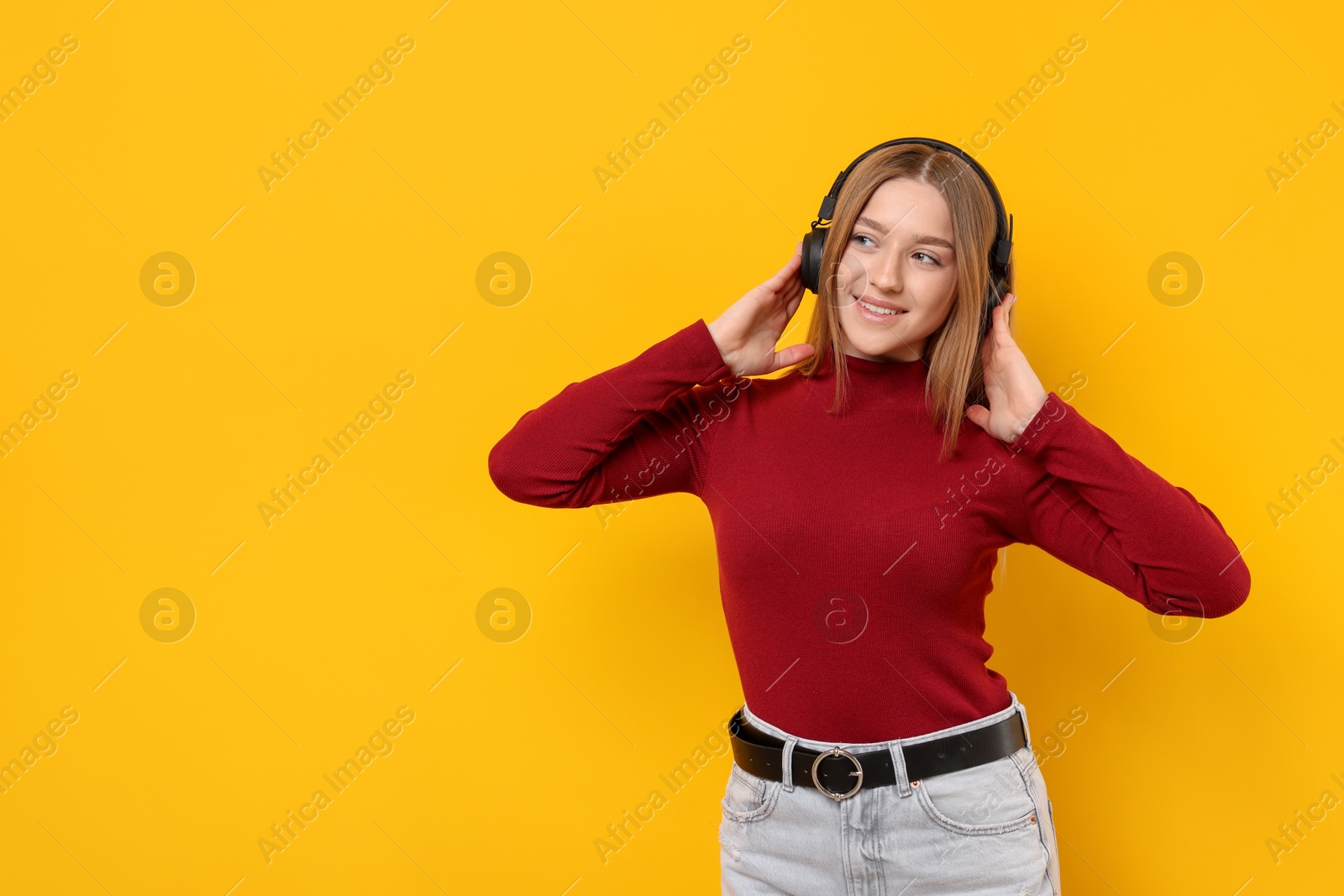 Smiling teenage girl in headphones listening to music on yellow background. Space for text Photo of Smiling teenage girl in headphones listening to music on yellow background. Space for text