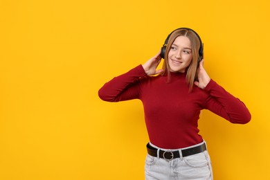 Photo of Smiling teenage girl in headphones listening to music on yellow background. Space for text