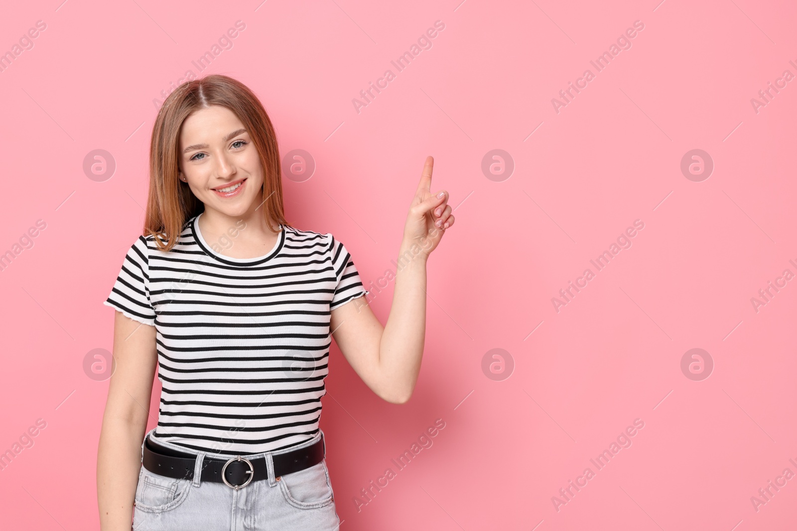 Portrait of smiling teenage girl pointing at something on pink background. Space for text Photo of Portrait of smiling teenage girl pointing at something on pink background. Space for text