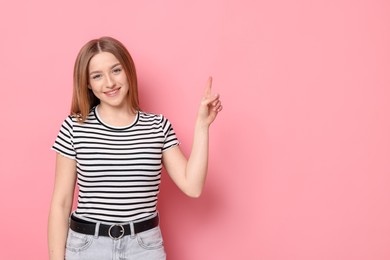 Photo of Portrait of smiling teenage girl pointing at something on pink background. Space for text