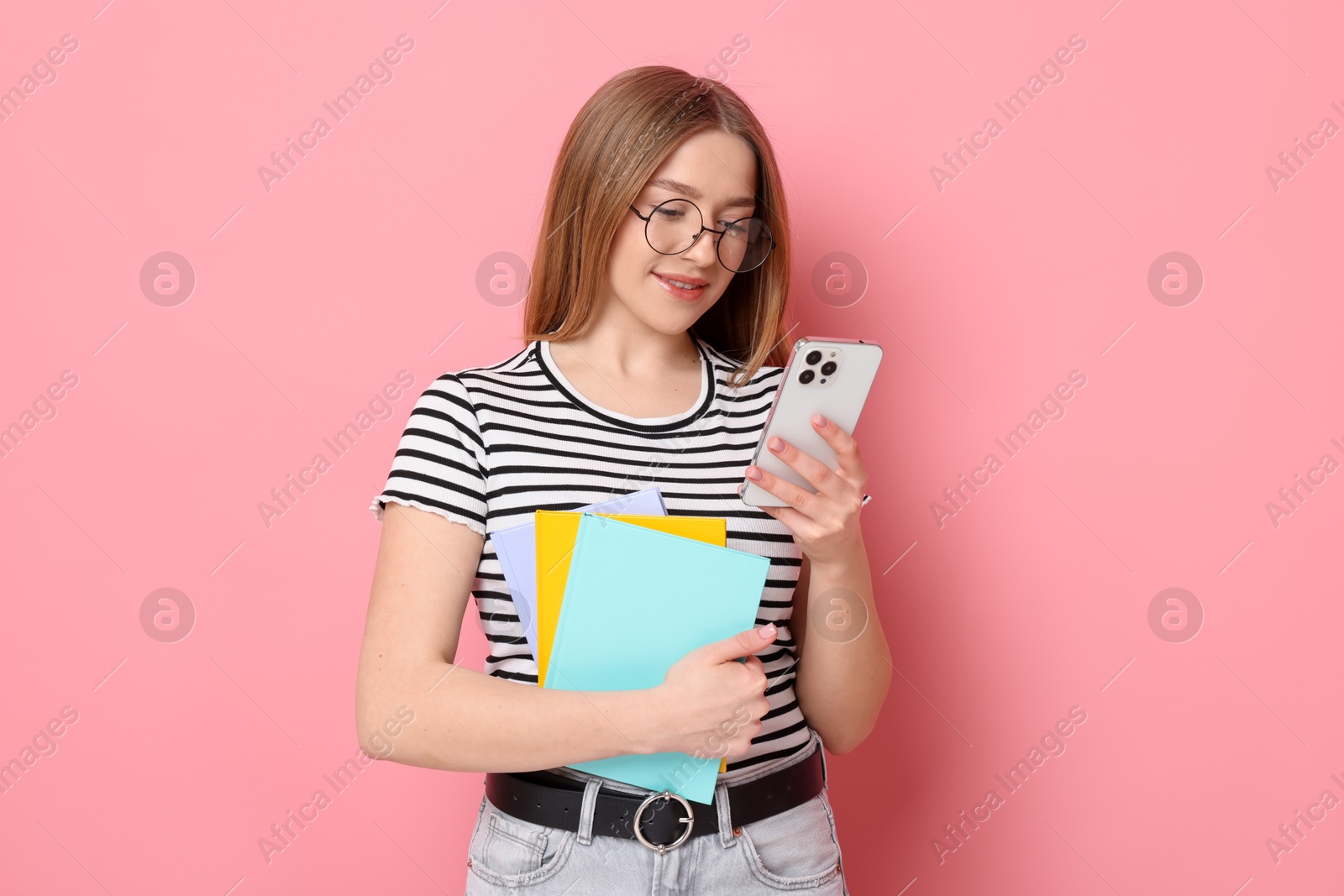 Smiling teenage girl with books and smartphone on pink background Photo of Smiling teenage girl with books and smartphone on pink background