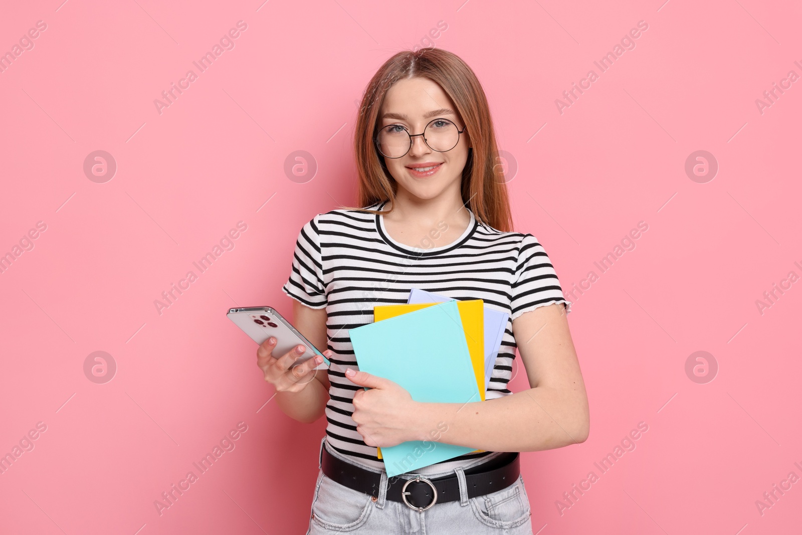 Smiling teenage girl with books and smartphone on pink background Photo of Smiling teenage girl with books and smartphone on pink background