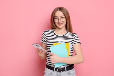 Photo of Smiling teenage girl with books and smartphone on pink background