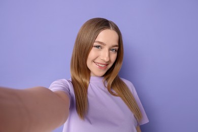 Photo of Smiling teenage girl taking selfie on violet background