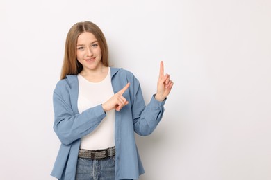 Photo of Portrait of smiling teenage girl pointing at something on white background. Space for text