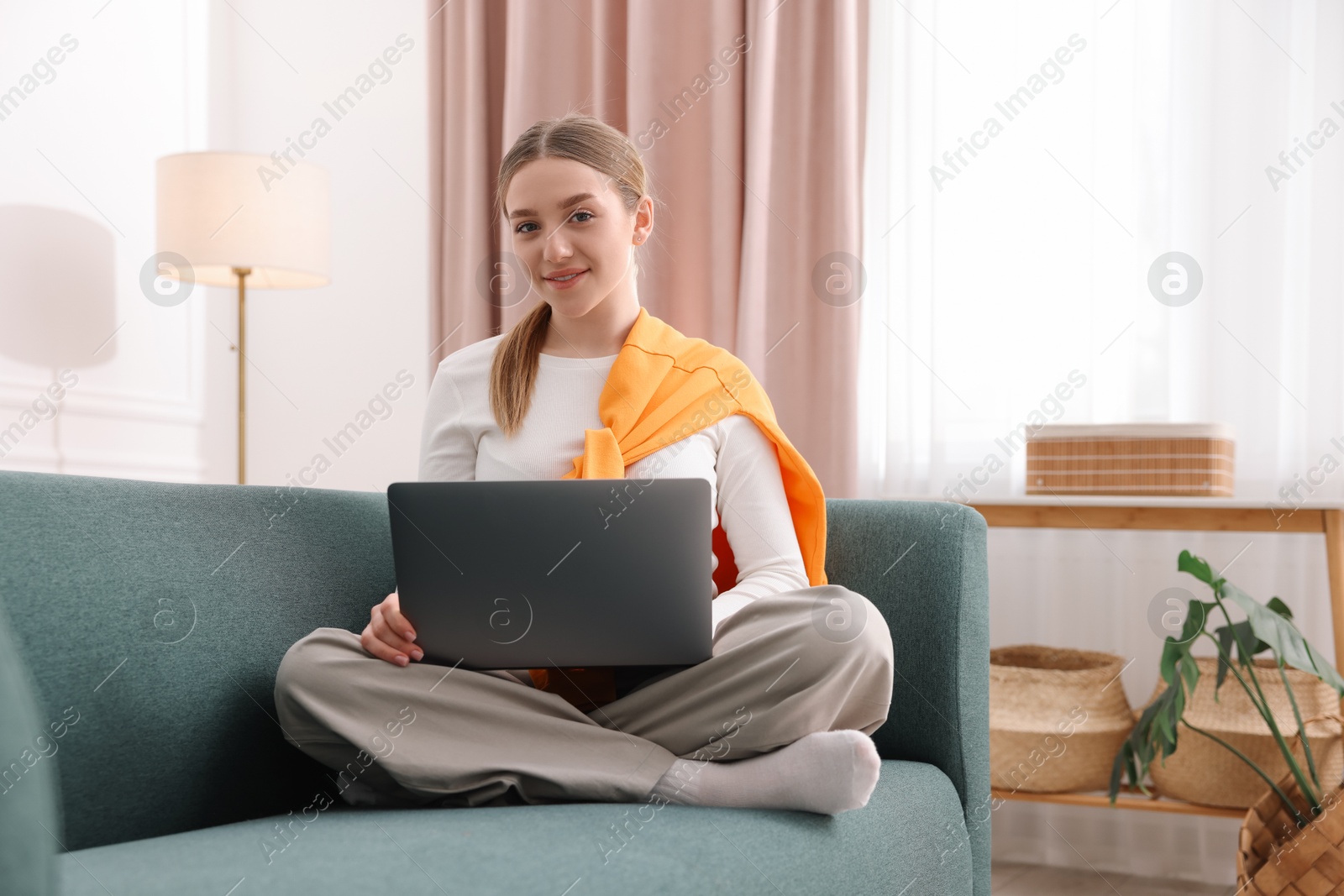 Smiling teenage girl with laptop on sofa at home Photo of Smiling teenage girl with laptop on sofa at home