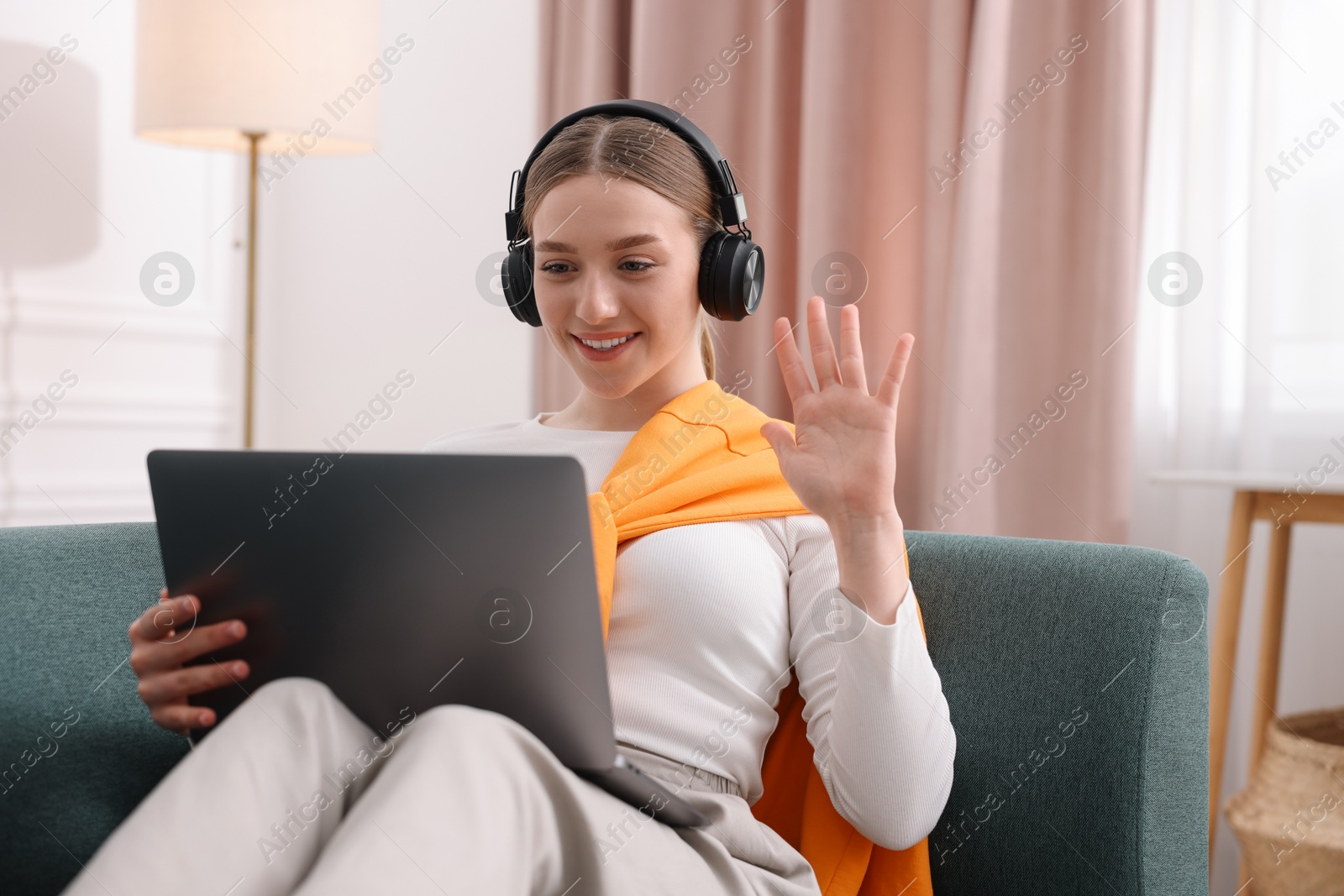 Smiling teenage girl in headphones having videochat by laptop on sofa at home Photo of Smiling teenage girl in headphones having videochat by laptop on sofa at home