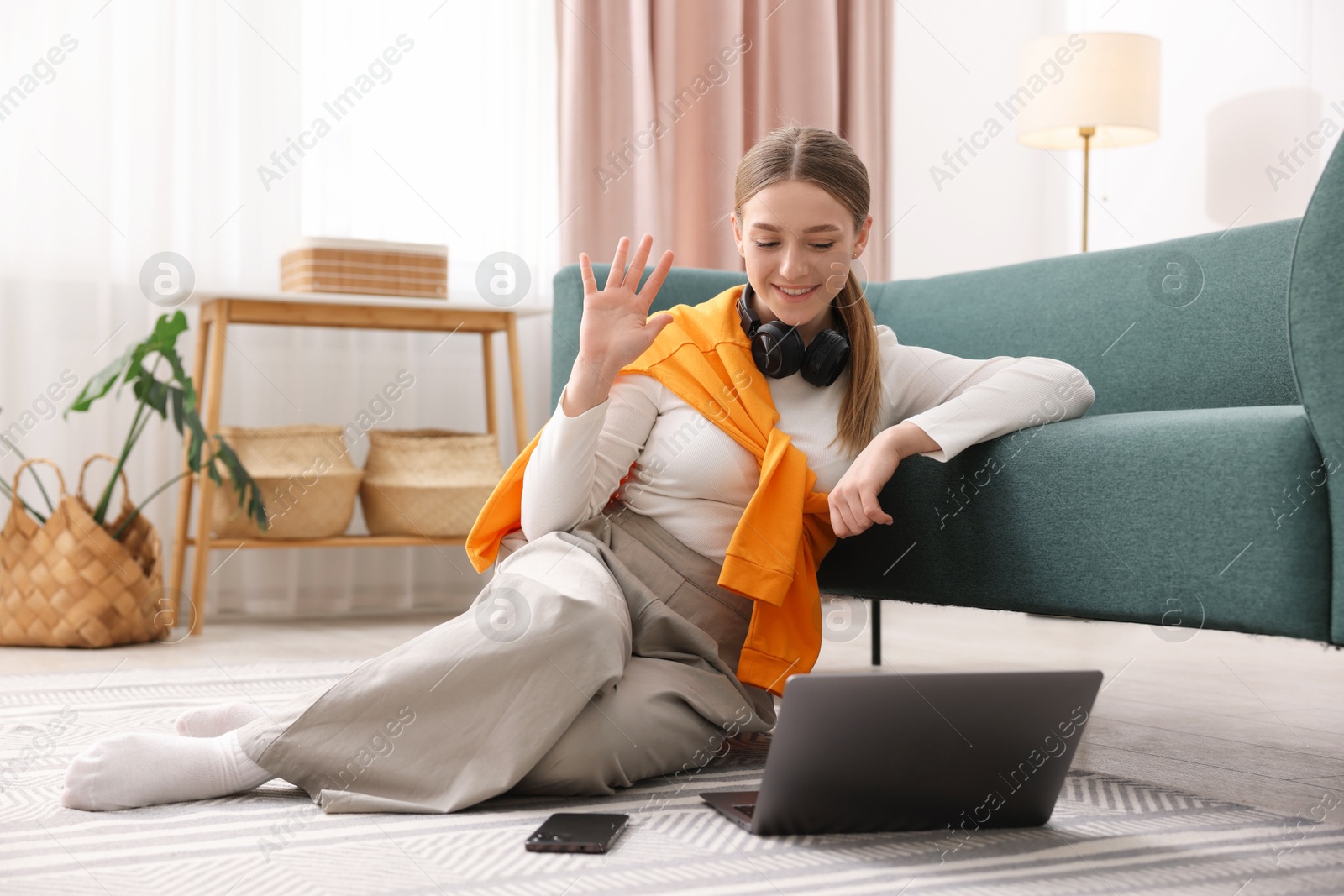 Smiling teenage girl having videochat by laptop on floor at home Photo of Smiling teenage girl having videochat by laptop on floor at home