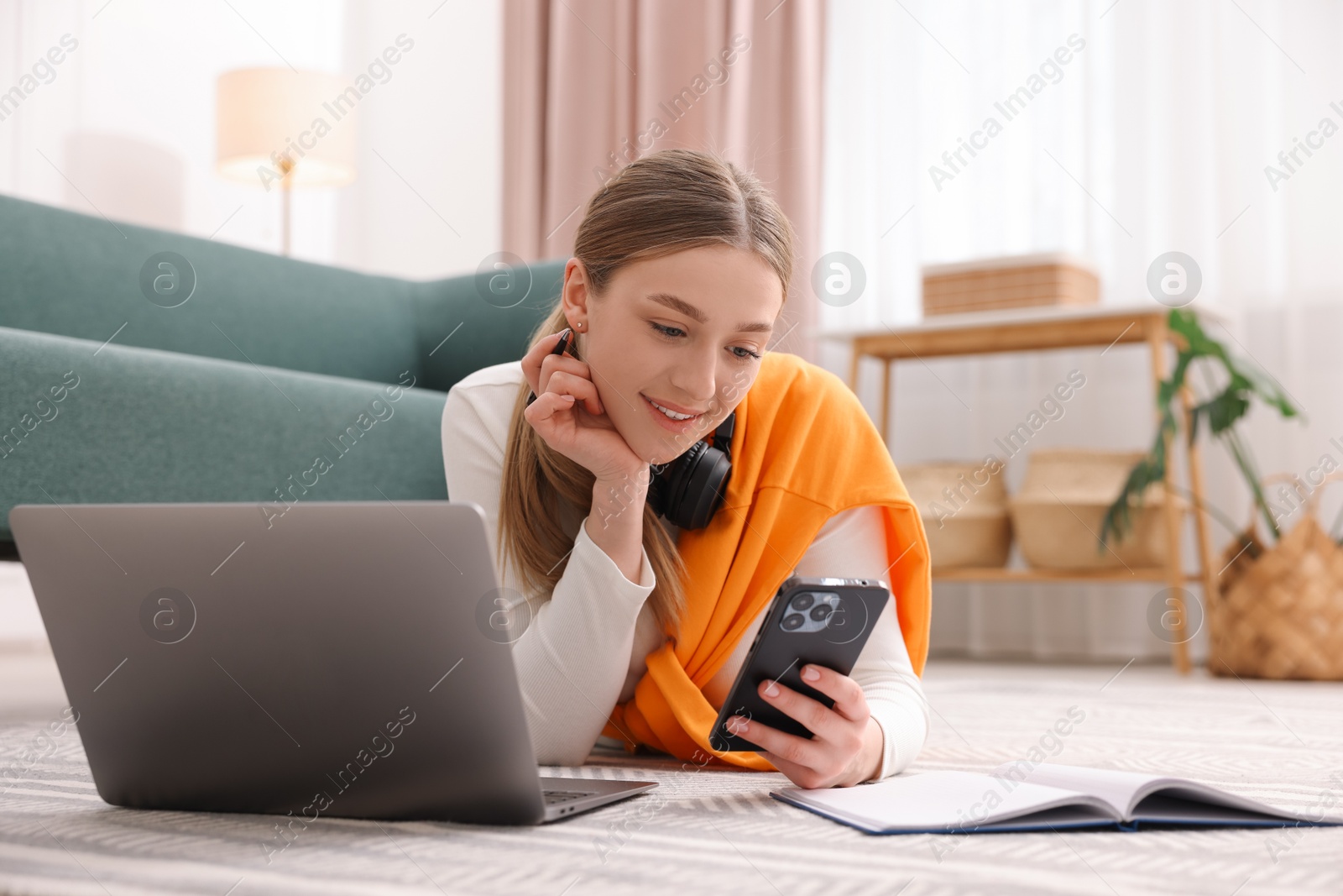 Smiling teenage girl with smartphone and laptop on floor at home Photo of Smiling teenage girl with smartphone and laptop on floor at home