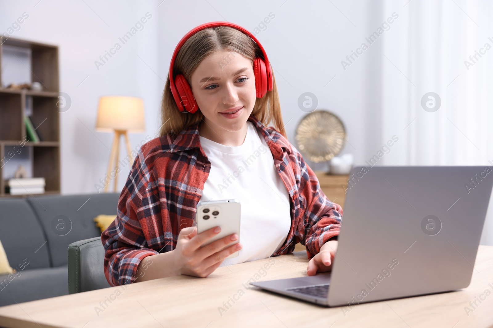 Smiling teenage girl with smartphone and laptop at table indoors Photo of Smiling teenage girl with smartphone and laptop at table indoors