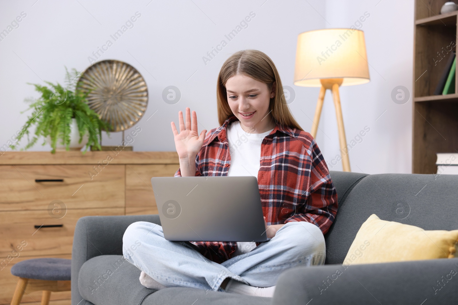 Smiling teenage girl having videochat by laptop on sofa at home Photo of Smiling teenage girl having videochat by laptop on sofa at home