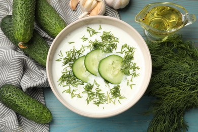 Photo of Tasty cucumber soup in bowl and ingredients on light blue wooden table, flat lay